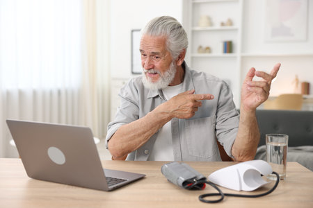 Senior man having online consultation with doctor via laptop at table indoors