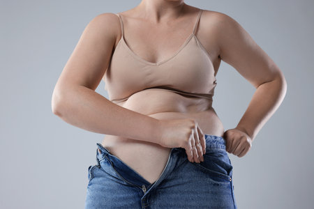 Liposuction. Woman trying to put on tight jeans against gray background, closeupの写真素材