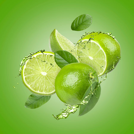 Fresh limes and drink splash in air against green background
