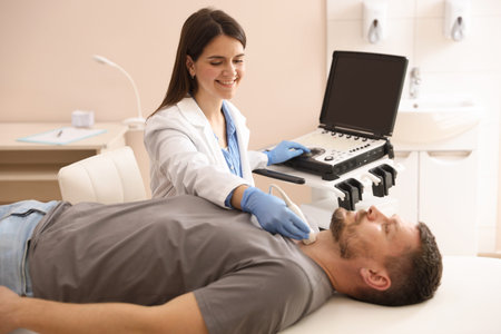 Sonographer conducting ultrasound examination of man's thyroid gland in clinic