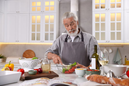 Elderly man cooking at table in kitchenの写真素材