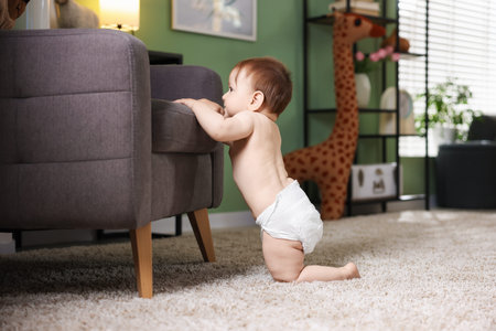 First steps. Cute little baby in diaper near sofa at home, space for text