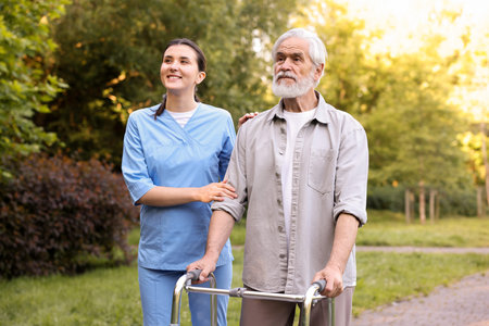 Smiling nurse supporting elderly man who using walking frame outdoorsの写真素材
