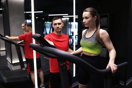 Young woman exercising on treadmill with professional personal trainer in gym