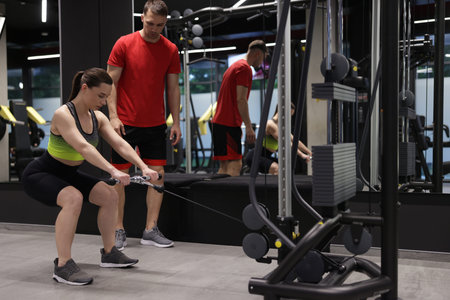 Young woman exercising with cable machine with professional personal trainer in gym