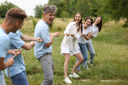 Team building. Group of happy people playing tug of war with rope outdoors