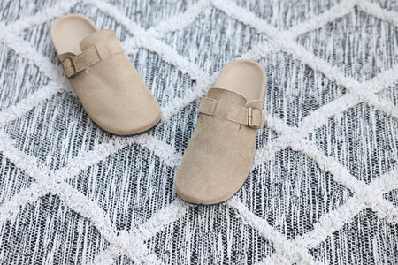 Stylish beige slippers on soft carpet with pattern
