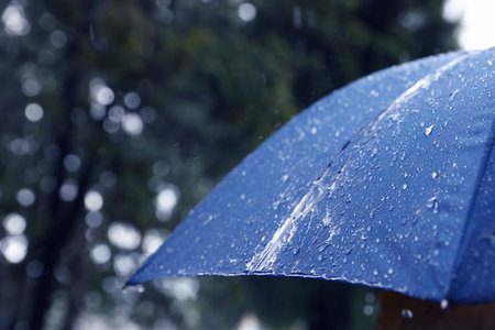 Blue umbrella under heavy rain outdoors, closeup. Space for text