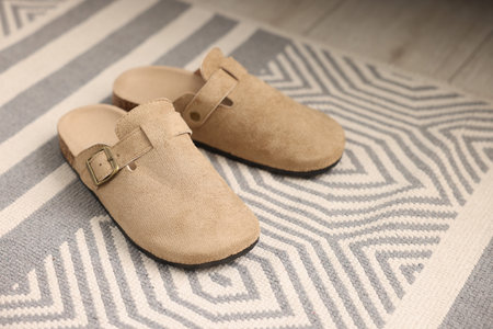 Stylish beige slippers on carpet with pattern, closeup