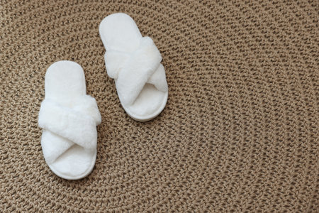 Fluffy white slippers on wicker mat, top viewの写真素材