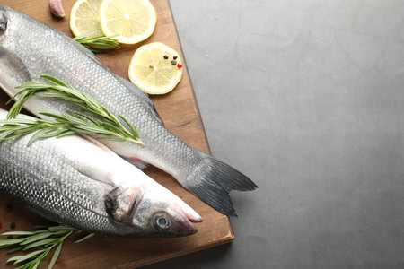 Fresh raw seabass fish with spices on grey table, top view and space for text. Seafood delicacies