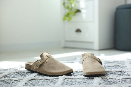 Stylish beige slippers on floor indoors, closeup. Space for text