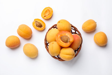 Fresh apricots and wicker basket on white background, flat lay