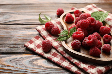 Tasty fresh ripe raspberries and leaves on wooden table, closeup. Space for text