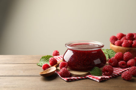 Tasty jam, fresh ripe raspberries and leaves on wooden table, closeup. Space for text
