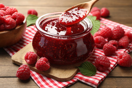 Taking tasty jam with spoon on wooden table, closeup