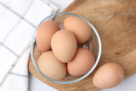 Raw eggs in bowl on white table, top view