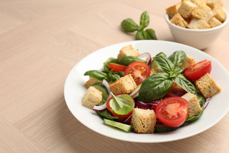 Delicious salad with croutons, vegetables and basil on wooden table, closeup. Space for text
