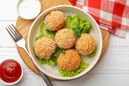 Delicious fried croquette balls with parsley, lettuce and sauces on white wooden table, flat lay