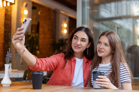 Mother and her teenage daughter taking selfie at table in cafeの写真素材