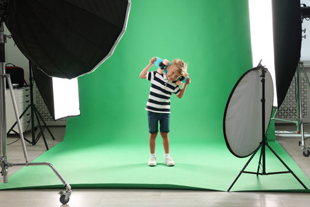 Little boy with board on green background in photo studio with professional equipmentの写真素材