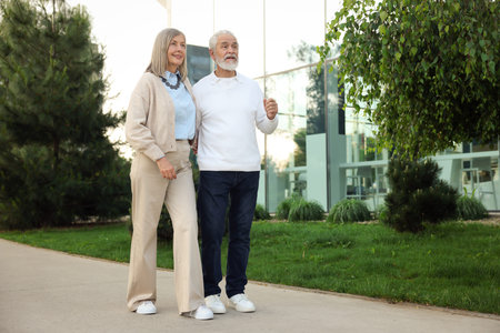 Lovely senior couple walking together near building outdoors, space for text