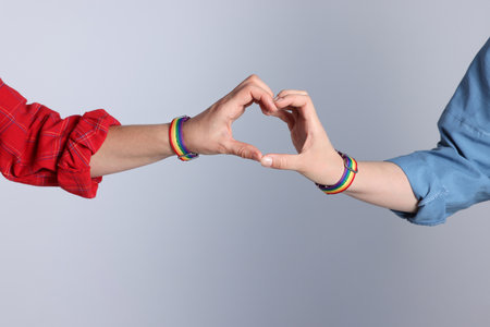 LGBT concept. Women in rainbow wristbands making heart shape on light gray background, closeupの写真素材
