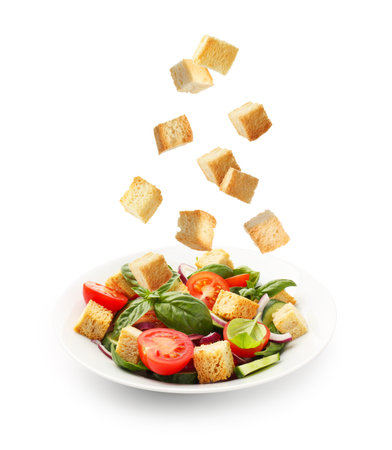 Croutons falling into bowl of salad against white backgroundの写真素材