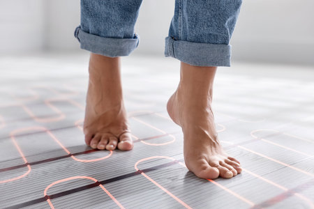 Woman walking barefoot on warm floor at home, closeup. Underfloor heating system seen through...