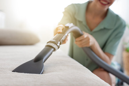 Woman cleaning sofa with vacuum cleaner at home, closeupの写真素材