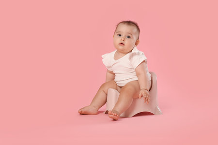 Cute little baby sitting on potty against pink background, space for textの写真素材