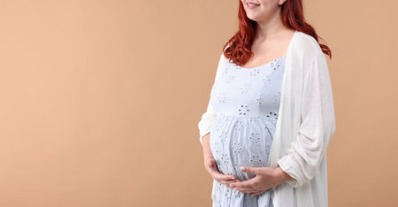 Pregnant woman on beige background, closeup. Space for text