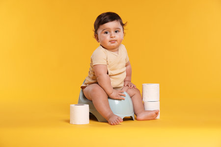 Cute little baby sitting on potty and rolls of toilet paper against orange backgroundの写真素材