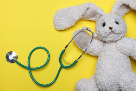 Pediatrics concept. Toy bunny with stethoscope on yellow background, top viewの写真素材