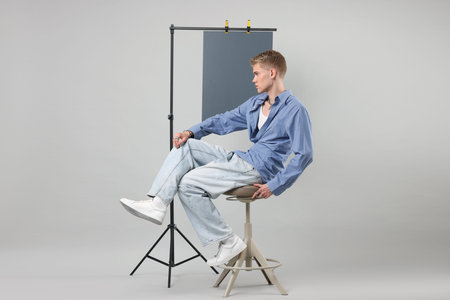 Handsome young man wearing stylish clothes sitting on chair against light grey background