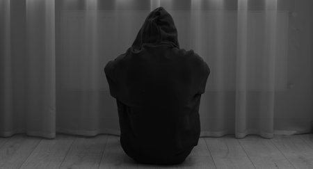 Sadness and depression. Silhouette of man in hoodie near curtains at home, back view. Black and white effectの写真素材