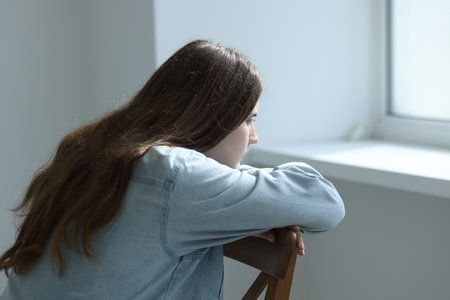 Sad young woman near window at homeの写真素材