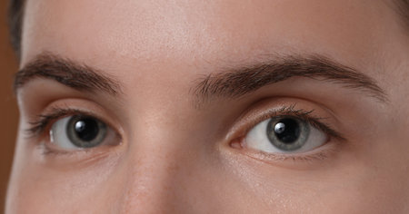 Young woman with beautiful eyebrows on brown background, closeup