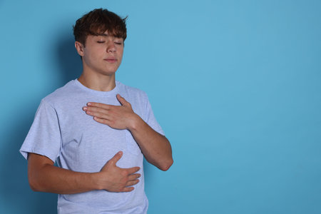 Teenage boy deep breathing on light blue background, space for text.