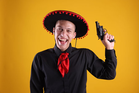 Happy man in black Flamenco hat with gun on yellow backgroundの写真素材