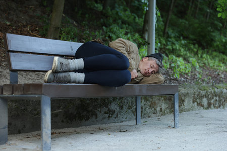 Homeless man sleeping on bench in park