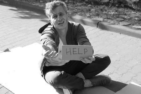 Homeless man with sign Help begging for money on carton outdoors. Black and white effect