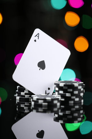 Casino chips and playing card on mirror surface against blurred lights, closeup