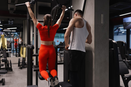 Young woman exercising with professional personal trainer in gym, back view
