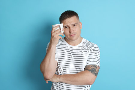 Man with cup of drink suffering from hangover on light blue backgroundの写真素材