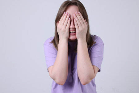Woman eyes covering with hands and laughing on gray backgroundの写真素材
