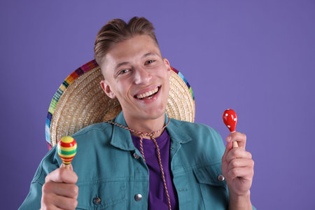 Happy man with sombrero hat playing maracas on purple background
