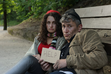 Homeless people with sign Help near bench in parkの写真素材