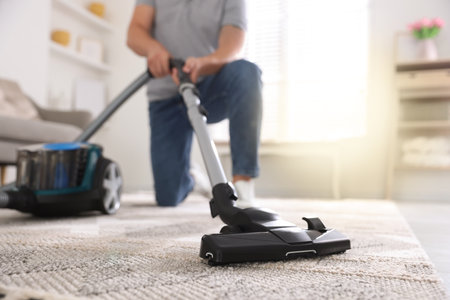 Man cleaning carpet with vacuum cleaner at home, closeupの写真素材