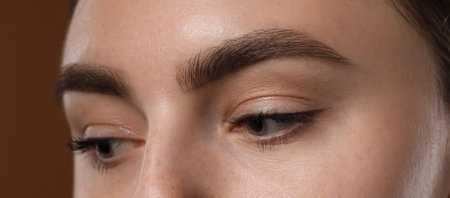 Young woman with beautiful eyebrows on brown background, closeup